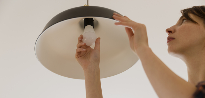 Woman about 25 years old, with her hand on an LED bulb in a chandelier